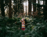 Little girl with binoculars looking up at trees bathed in sunlight in the forest