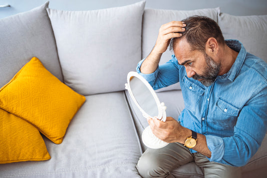 Middle-aged man looking at a mirror, upset with thinning hair  