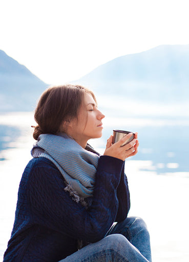 Woman relaxes by a misty lake drinking her morning coffee