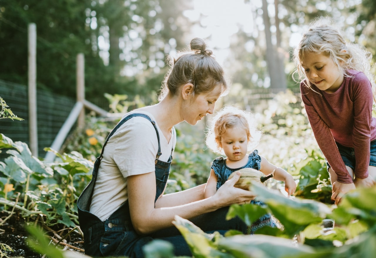 Mother sitting in a quiet garden with her two young children, teaching them how to garden